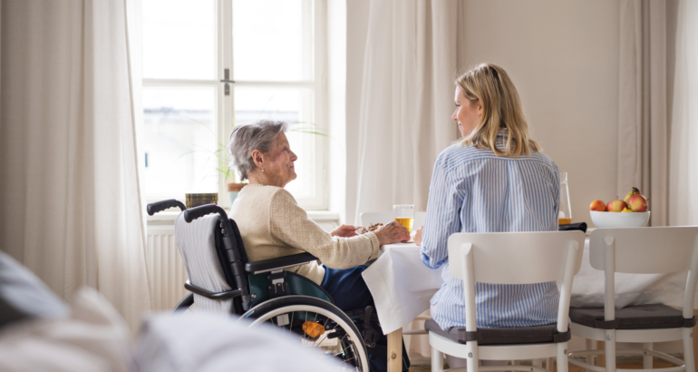 A senior woman in wheelchair with a health visitor sitting at the table at home.