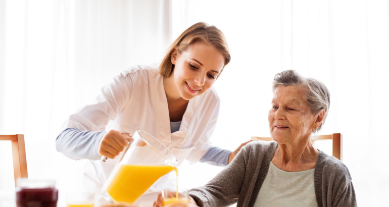 Health visitor and a senior woman during home visit. Health visitor and a senior woman during home visit. A nurse pouring orange juice to and an elderly woman.